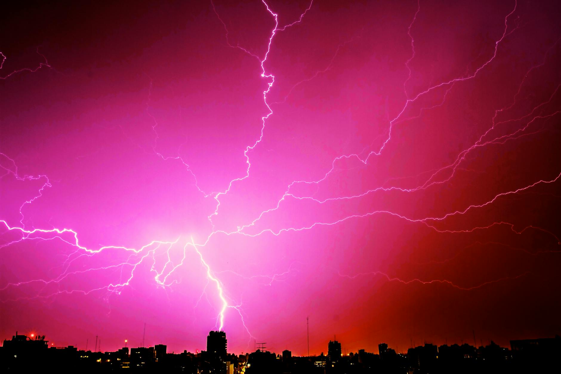 A lightning strike hitting a city in silhouette, creating a pink lighting effect. 